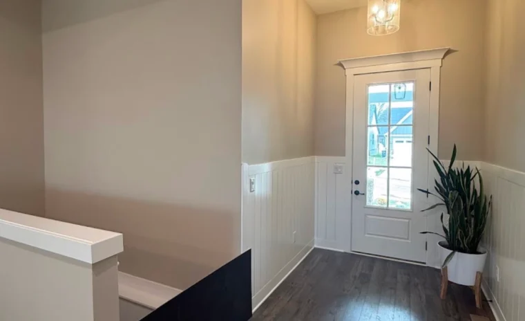 An entryway features white wainscoting on beige walls